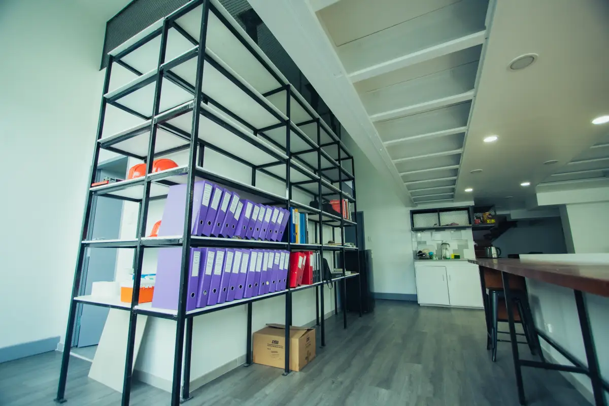 Office storage shelving with organized binders next to a break room area